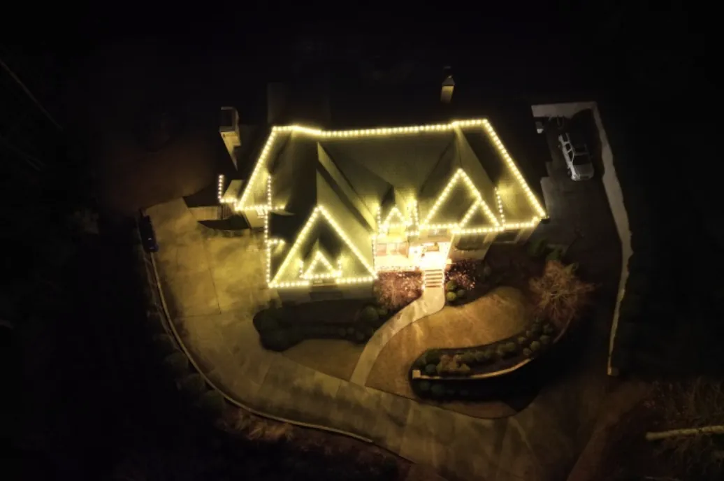 Overhead view of several roof peaks outlined in warm white lights.