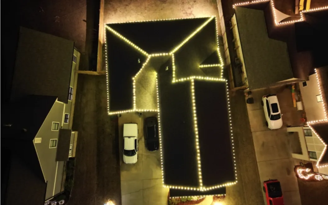 Overhead view of a house roof outlined in warm white Christmas lights at night.