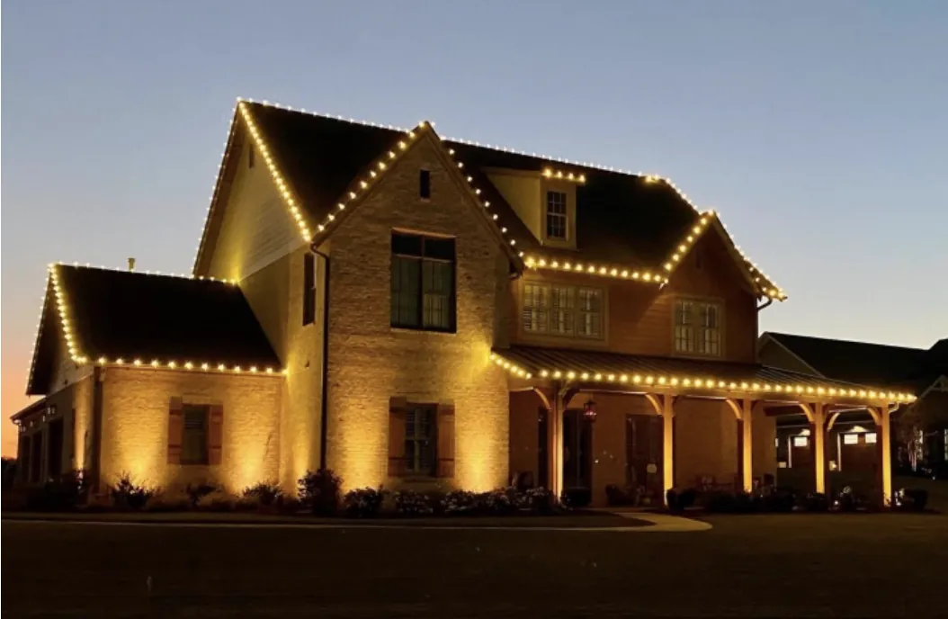 Roofline and porch lights on a brick home with a covered porch at dusk.