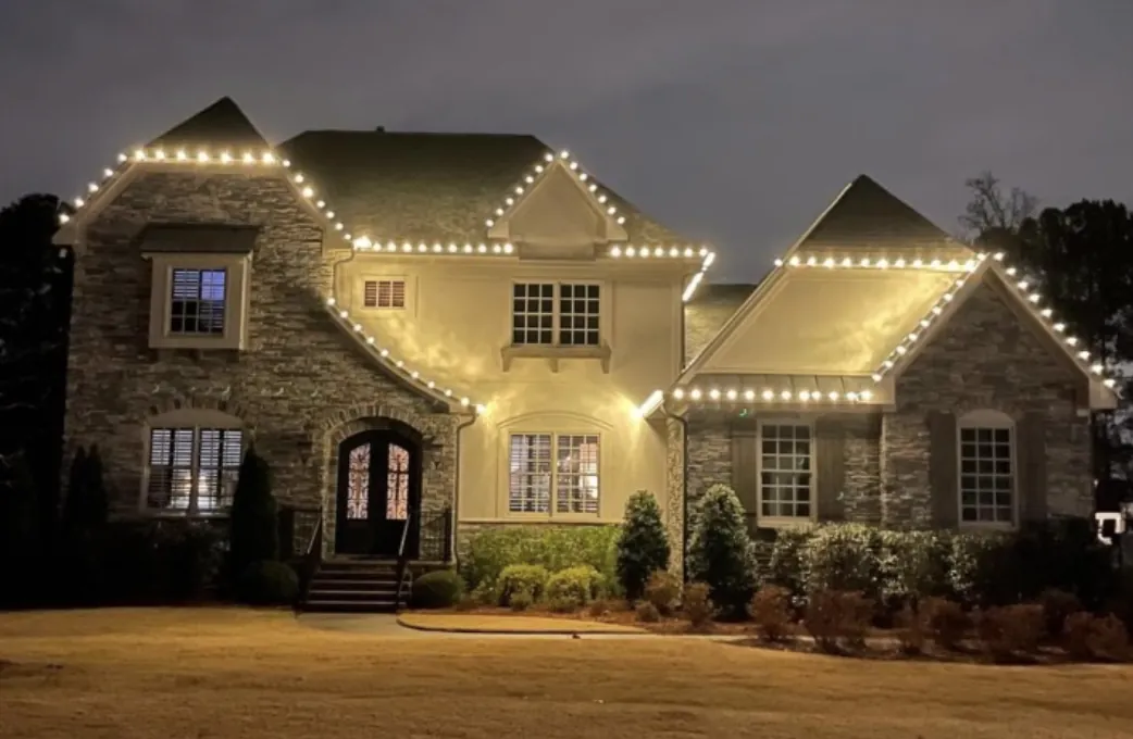 Roofline lights on a stone and stucco two-story home at dusk.